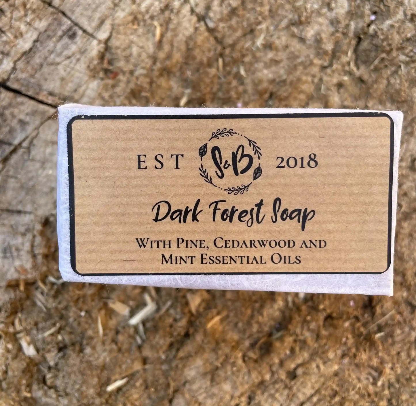 A bar of handmade travel size pine and cedarwood soap on a natural wood block.
